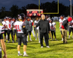 Holy Cross football players gather around their coach on the field at Trimble County during Week 9 of the 2026 high school football season.